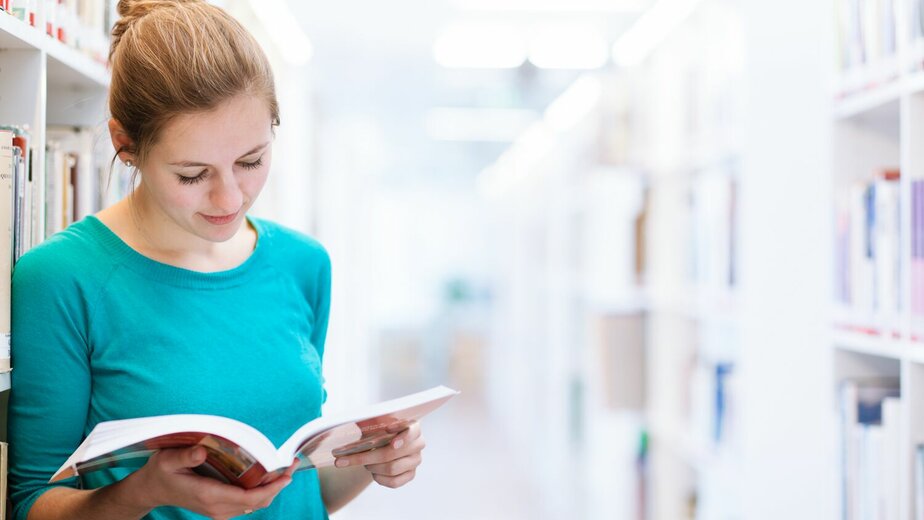 Vrouw leest boek in bibliotheek